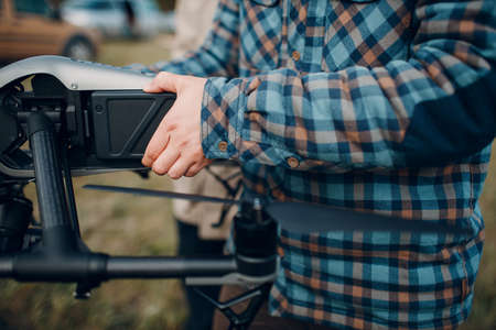 Man pilot checking quadcopter drone battery replacement and charging before aerial flight and filmingの写真素材