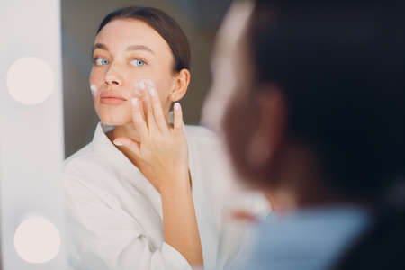 Young woman applying cosmetic white cream on faceの写真素材