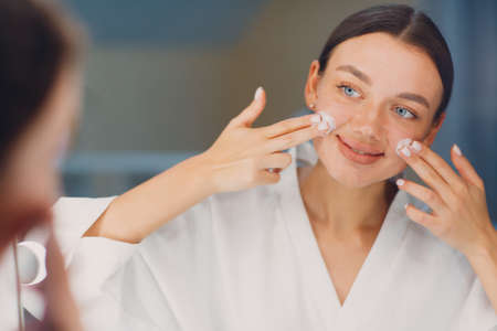Young woman applying cosmetic white cream on faceの写真素材