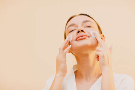 Young woman applying cosmetic white cream on faceの写真素材