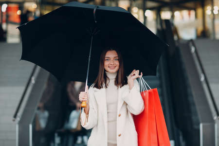 Positive young adult woman carrying paper shopping bags and umbrella in hands.の写真素材
