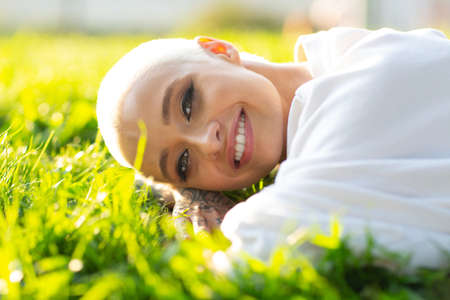Portrait of young smiling millenial european short haired woman lying on green grass meadow summer park. Beautiful happy blonde girl outdoorsの写真素材