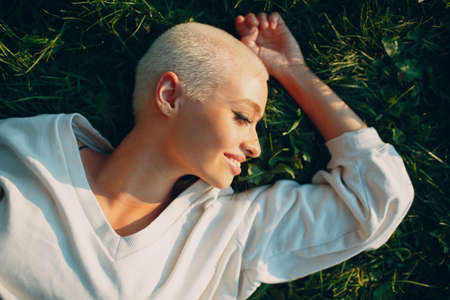 Portrait of young smiling millenial european short haired woman lies on green grass meadow summer park overhead top aerial view. Beautiful happy blonde girl outdoorsの写真素材