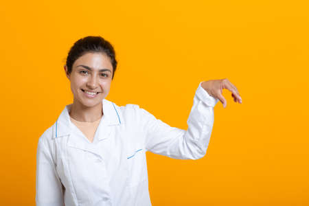 Portrait of indian doctor woman in white medical gown holding fingers template vaccine covid-19 or other medical stuff isolated on yellow background.の写真素材