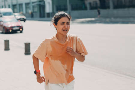 Young indian woman runner jogging in wet sweaty t-shirt at city street urbanの写真素材