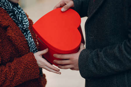 A guy gives his girlfriend giving heart-shaped box close up in Valentines Day. Young couple at shopping mallの写真素材