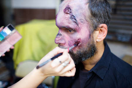 Zombie male makeup applying for halloween concept. Make up with brush and paint skin and blood faceの写真素材