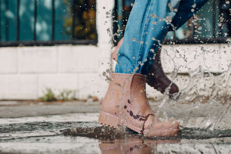 Woman wearing rain rubber boots walking running and jumping into puddle with water splash and drops in autumn fallの写真素材