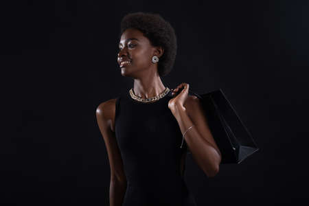 African american woman with afro hairstyle holds black shopping bags. Sale and discounts on market going Black Friday concept.の写真素材