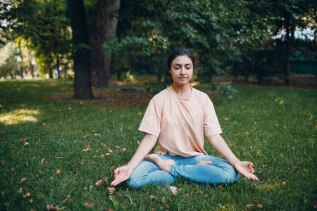 Indian woman doing yoga and meditation in lotus asana pose in outdoor summer park.の写真素材