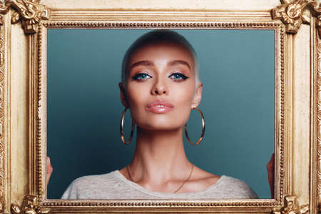 Young adult woman face beauty portrait with short blonde hair hold on gilded picture frameの写真素材
