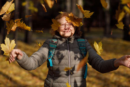 Adult mature fall woman throw up autumn leaves outside in colorful fall parkの写真素材