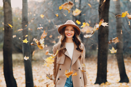 Young woman model in autumn park throw up yellow foliage maple leaves. Fall season fashionの写真素材