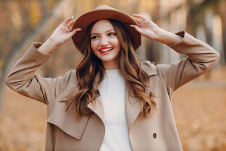 Young woman model in autumn park with yellow foliage maple leaves. Fall season trench coat fashionの写真素材