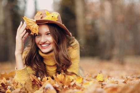 Young woman model lying in autumn park with yellow foliage maple leaves. Fall season fashionの写真素材