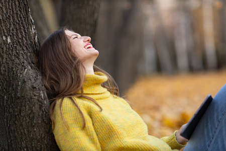 Young woman model online shopping outdoor with digital tablet pc in autumn park with yellow foliage maple leaves. Fall season fashion conceptの写真素材