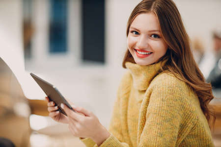 Beautiful young smiling woman online shopping with digital tablet at home kitchen tableの写真素材
