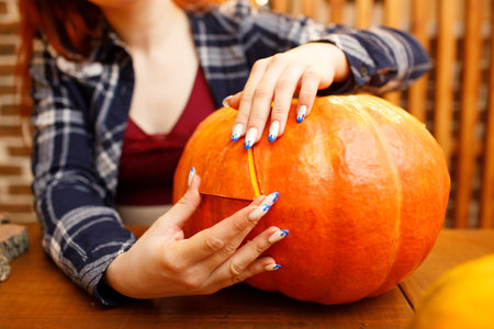 Young woman making Halloween pumpkin Jack-o-lantern. Female hands cutting pumpkins with knifeの写真素材