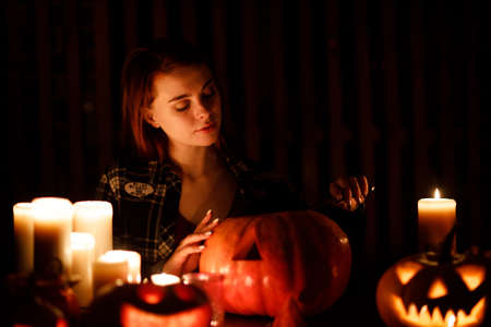 Young woman making Halloween pumpkin Jack-o-lantern with candles in dark. Female hands cutting pumpkins with knifeの写真素材