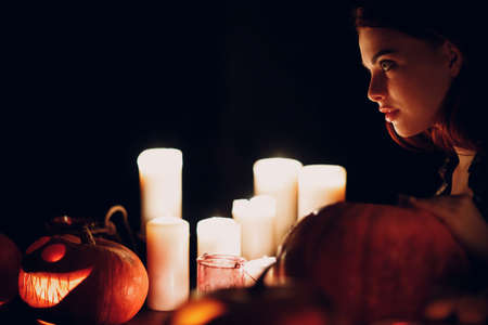 Young woman making Halloween pumpkin Jack-o-lantern with candles in darkの写真素材