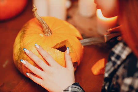 Young woman making Halloween pumpkin Jack-o-lantern with candles. Female hands cutting pumpkins with knifeの写真素材