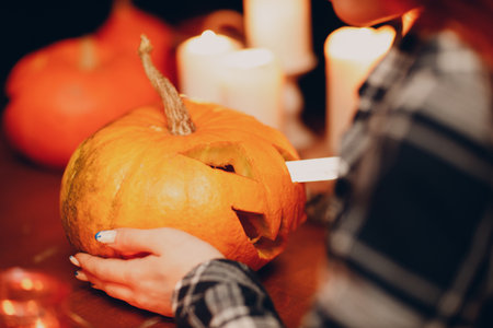 Young woman making Halloween pumpkin Jack-o-lantern with candles. Female hands cutting pumpkins with knifeの写真素材