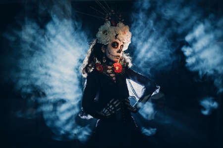 Woman with mexican skull halloween makeup in dark with backlight rays. Day of the dead aka Dia de los Muertos and halloween concept.の写真素材