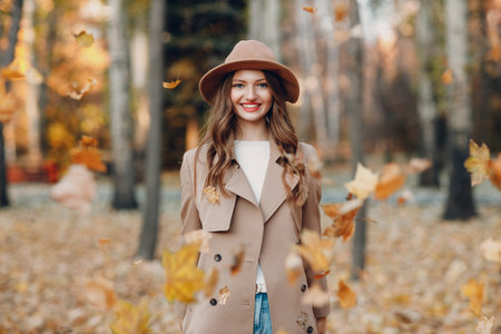 Young woman model in autumn park with yellow foliage maple leaves. Fall season fashion coat trenchの写真素材