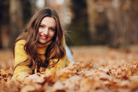 Young woman model lying in autumn park with yellow foliage maple leaves. Fall season fashionの写真素材