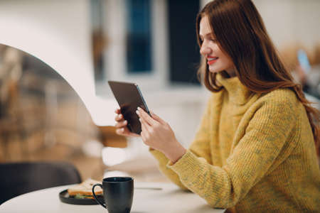 Beautiful young smiling woman online shopping with digital tablet at cafe table with cup of coffee.の写真素材