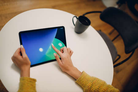 Beautiful young woman using digital tablet at cafe table with cup of coffee.