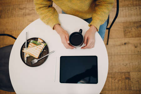 Beautiful young woman using digital tablet at cafe table with cup of coffee. Overhead top view.の写真素材