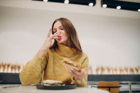Young european woman lick finger after eating sandwich at indoor cafe. Health and diet.の写真素材