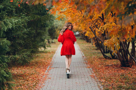 Young woman in red dress riding electric scooter in autumn city. Alternative commuter transportation.の写真素材