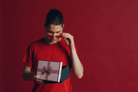 Cute guy with gift box on red background. Young man holding christmas gift box present. Cute surprised boy on red background.の写真素材