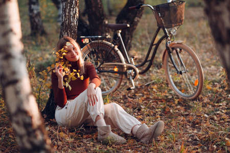 Happy active young woman riding vintage bicycle in autumn park at sunset.の写真素材