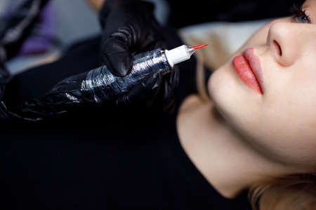 Cosmetologist applying red permanent make up tattoo on young woman lips.の写真素材