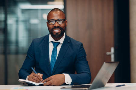 Portrait smiling african american businessman signs contract sit at table for meeting in office with notebook with pen and laptopの写真素材