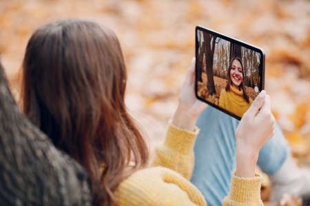 Young woman model take selfie photo with Apple iPad Pro 2021 tablet pc in autumn parkの写真素材
