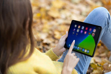 Young woman model sitting with tablet pc in autumn park with yellow foliage maple leaves. Fall season fashionの写真素材