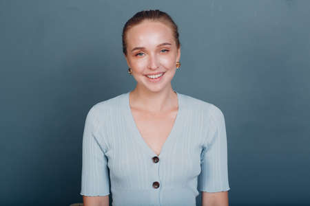 Portrait of young smiling european woman. Beautiful happy blonde girl wears t-shirt and looks at camera. Studio shoot isolated on blue background.の写真素材