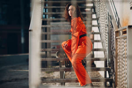 Young brunette curly woman in orange suit. Female in colorful overalls portraitの写真素材
