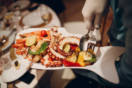 a waiter in a restaurant holds seafood dishes and serves a table catering Concept Healthy food octopus and crabs shellfish.の写真素材