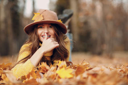 Young woman model lying in autumn park with yellow foliage maple leaves. Fall season fashionの写真素材