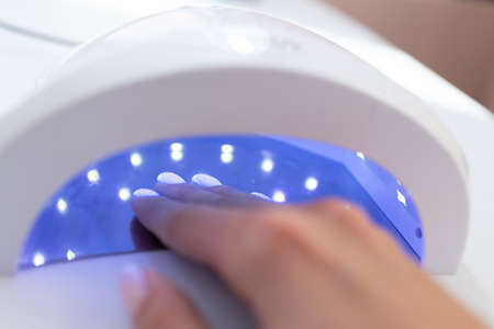 Female hand inside drying UV light machine in nail salon.の写真素材