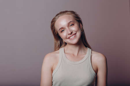 Portrait of young 20-25s years smiling european woman. Beautiful happy blonde girl wears t-shirt and looks at camera. Studio shoot isolated on pink background.の写真素材