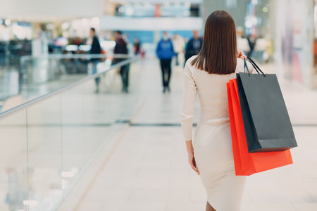 Positive young adult woman carrying paper shopping bags. Rear back viewの写真素材