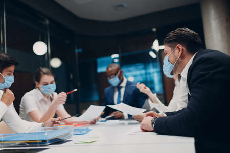 Businessman and businesswoman team in medical face mask at office meeting. Business people group conference discussion with boss.の写真素材