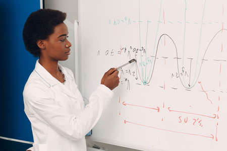 African American woman math teacher writing on blackboard with marker.の写真素材