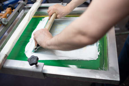 Serigraphy silk screen print process at clothes factory. Frame, squeegee and plastisol color paints.の写真素材